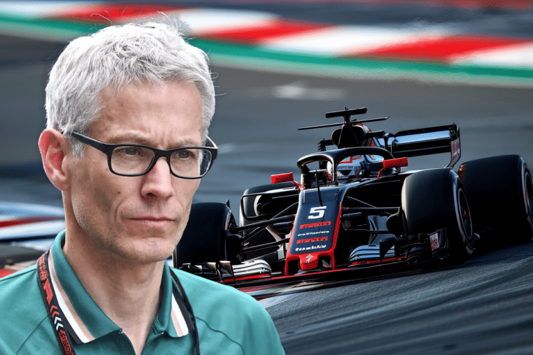 A composite image showing a serious-looking man with gray hair and glasses, wearing an Aston Martin lanyard, in the foreground. In the background, a black and red Haas Formula 1 car is racing on a track, turning into a curve with visible motion blur.