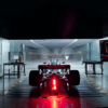 Inside Aston Martin’s Formula 1 facility, a dramatic and tense atmosphere surrounds the team’s wind tunnel, which sits idle with red warning lights flashing. Technical screens display airflow data and simulation errors, highlighting a critical malfunction. Engineers are absent, emphasizing the stillness and gravity of the situation. In the background, the 2025 Aston Martin F1 car remains untouched, its development halted. The scene conveys uncertainty and pressure, capturing the fragile state of the team’s season due to a failed wind tunnel system