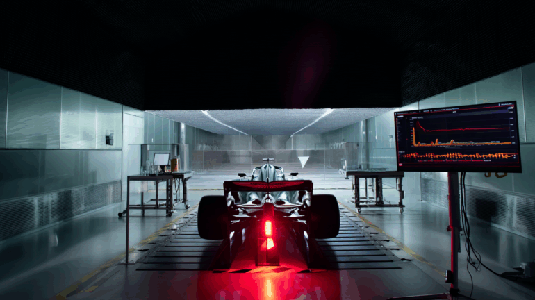 Inside Aston Martin’s Formula 1 facility, a dramatic and tense atmosphere surrounds the team’s wind tunnel, which sits idle with red warning lights flashing. Technical screens display airflow data and simulation errors, highlighting a critical malfunction. Engineers are absent, emphasizing the stillness and gravity of the situation. In the background, the 2025 Aston Martin F1 car remains untouched, its development halted. The scene conveys uncertainty and pressure, capturing the fragile state of the team’s season due to a failed wind tunnel system