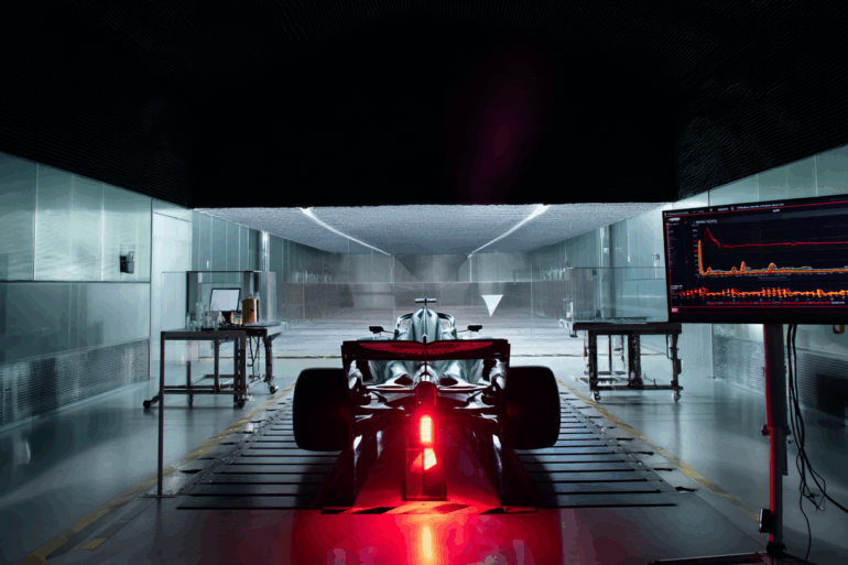 Inside Aston Martin’s Formula 1 facility, a dramatic and tense atmosphere surrounds the team’s wind tunnel, which sits idle with red warning lights flashing. Technical screens display airflow data and simulation errors, highlighting a critical malfunction. Engineers are absent, emphasizing the stillness and gravity of the situation. In the background, the 2025 Aston Martin F1 car remains untouched, its development halted. The scene conveys uncertainty and pressure, capturing the fragile state of the team’s season due to a failed wind tunnel system