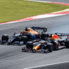A Red Bull Formula 1 car races past a McLaren on a high-speed track corner, with visible sparks trailing behind the Red Bull car. The intense moment captures the action of a competitive overtake during a Formula 1 Grand Prix. ​