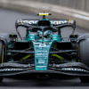 Max Verstappen driving an Aston Martin Formula 1 car at high speed on a racetrack. He’s wearing a green Aston Martin race suit and custom helmet, tightly seated in the cockpit as he takes a sharp corner. The car features the iconic metallic British racing green livery, gleaming under track lighting. The scene is dramatic and unexpected, suggesting a bold shift in F1 dynamics
