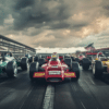 A lineup of vintage Formula 1 cars on the starting grid of a racetrack, ready for a race. The scene is dramatic with dark clouds in the sky, grandstands full of spectators, and an American flag waving in the background. The image highlights the classic design and color schemes of historic racing cars.